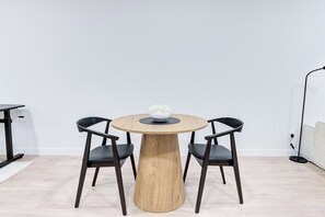 A round wooden table with two black chairs, a white bowl with flowers, and a white wall. - Hygge Hideaway –  Near the River (30 Nights +) (Saskatoon)