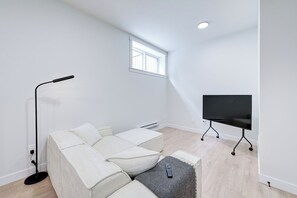 A modern, minimalistic room with a sectional sofa, a standing floor lamp, a flat-screen TV, and a small window.