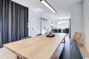A modern kitchen with a central island, a dining area with a long table, and a view of the adjacent living space. - Hygge Haven – Stylish Stay near the River (Saskatoon)