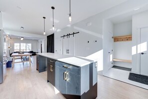 A modern kitchen with a central island, pendant lighting, and a dining area with a table and chairs. - Hygge Haven – Stylish Stay near the River (Saskatoon)