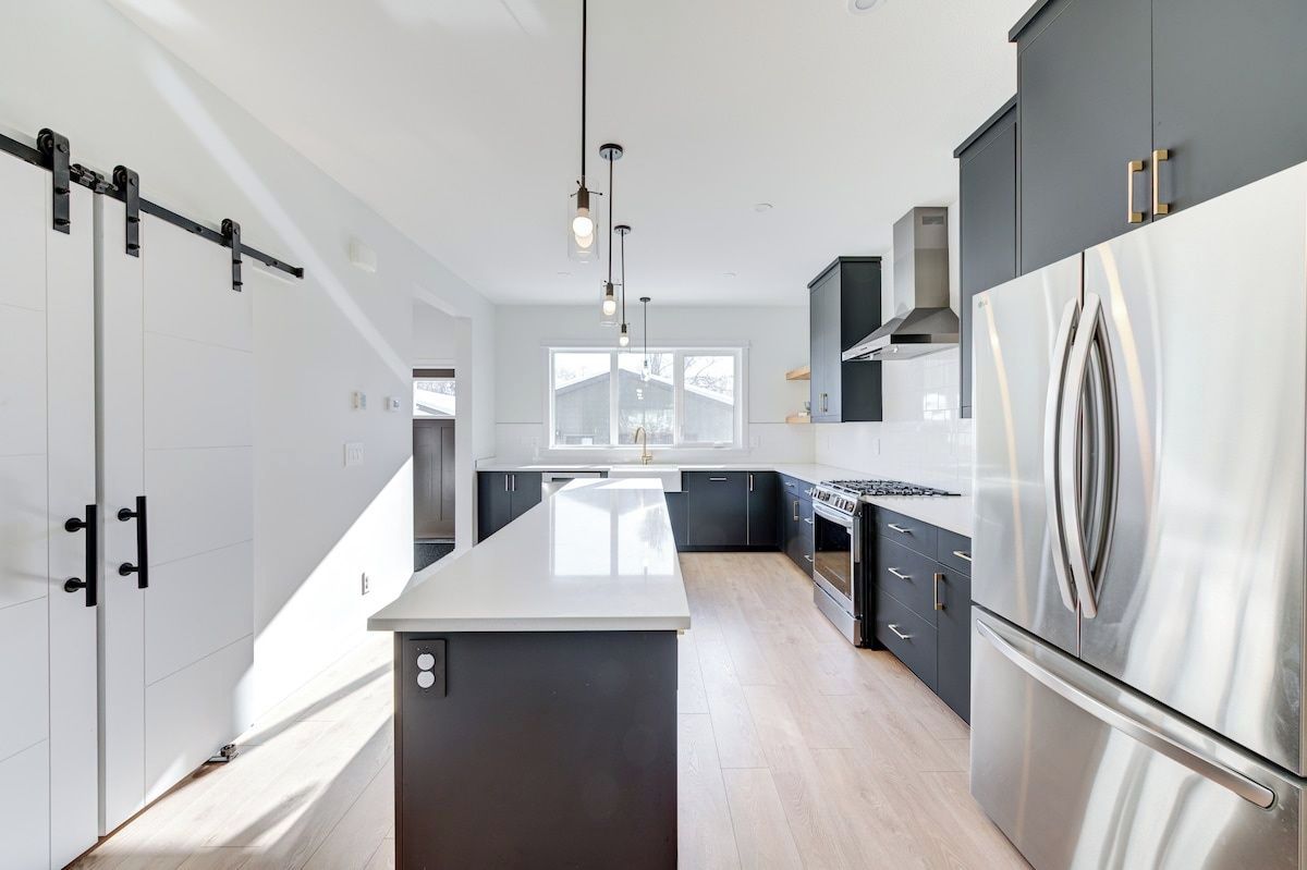 A modern kitchen with a central island, stainless steel appliances, and a view to the outside.