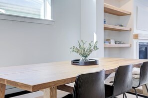 Un comedor moderno con una mesa de madera, sillas negras, un florero con follaje y estantes empotrados con objetos.