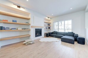 Una sala de estar moderna con chimenea, estantes empotrados, un sofá seccional gris y un ventanal grande.