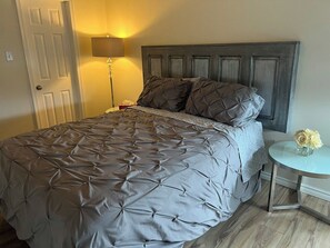 A bed with a grey quilted bedspread and a wooden headboard. - The Magnolia - 2BDR Condo Downtown (Saskatoon)