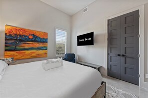 Quarto de hotel com cama, quadro, televisão e porta.