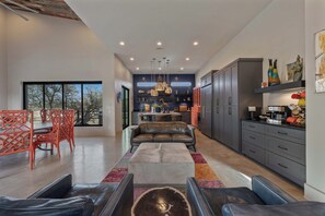 A modern kitchen with dark cabinets, a dining area with a red chair, and a large window. - Lake Buchanan Bliss | Pool & Spa • Lakefront Beach (Burnet)