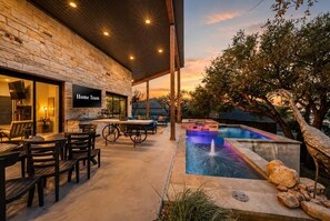 A covered outdoor area with a pool, seating, and a stone wall. - Lake Buchanan Bliss | Pool & Spa • Lakefront Beach (Burnet)
