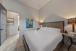 A hotel room with a large bed, a wooden headboard, a painting on the wall, a bedside lamp, and a small table with a lamp. - Lake Buchanan Bliss | Pool & Spa • Lakefront Beach (Burnet)