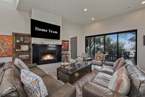 A modern living room with a fireplace, comfortable seating, and a large window overlooking a scenic view. - Lake Buchanan Bliss | Pool & Spa • Lakefront Beach (Burnet)