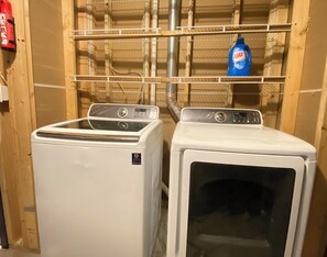 A laundry room with two white dryers, a blue detergent bottle on a shelf, and a fire extinguisher on the left. - Luxury 6BR Retreat - Spacious & Refined Living (Apple Valley)