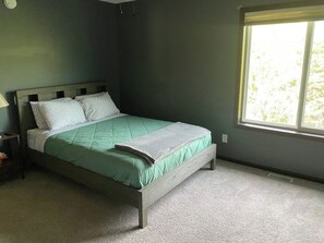 A bedroom with a bed, a nightstand, a window, and a carpeted floor. - Luxury 6BR Retreat - Spacious & Refined Living (Apple Valley)