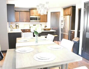 A modern kitchen with wooden cabinets, stainless steel appliances, and a dining table set for four. - Luxury 6BR Retreat - Spacious & Refined Living (Apple Valley)