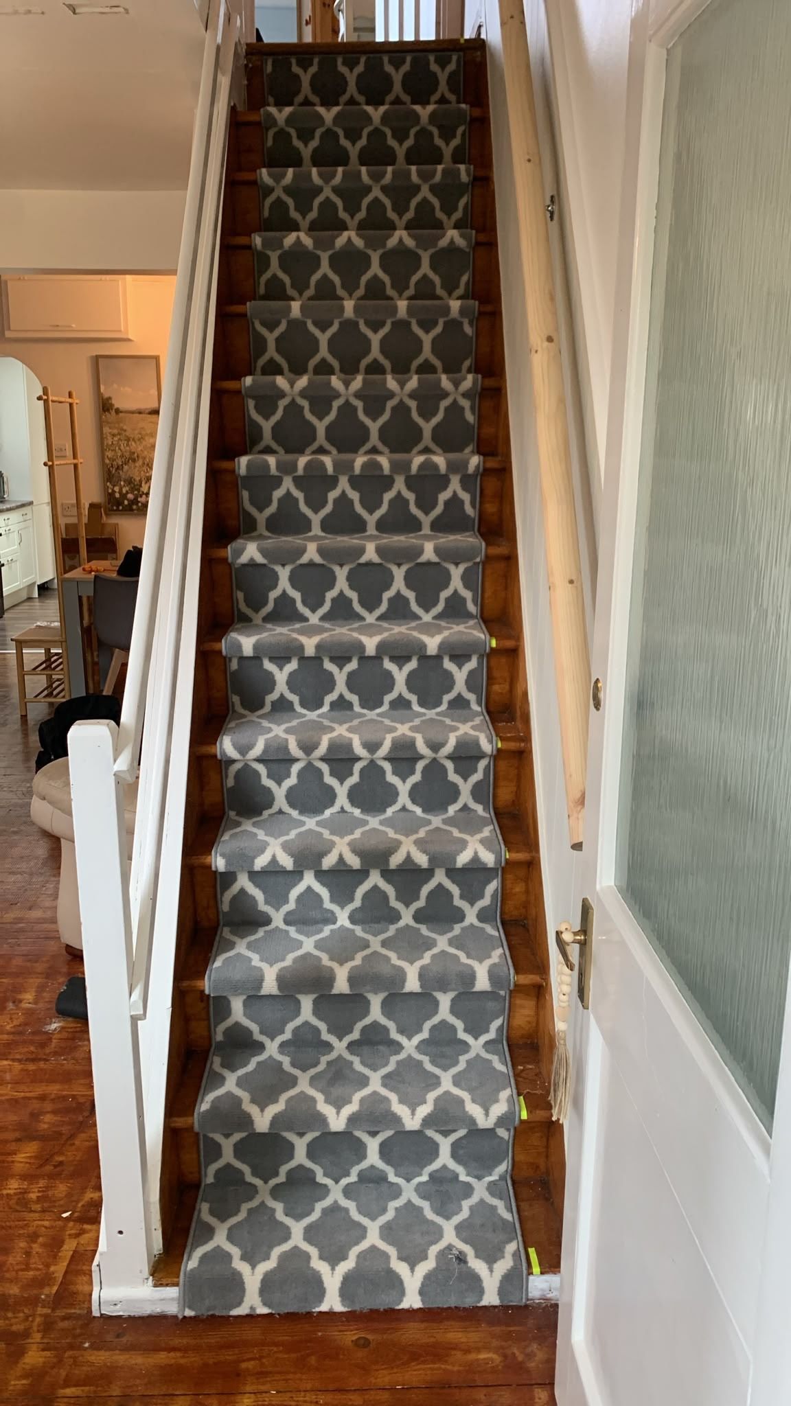 Una escalera con alfombra estampada, peldaños de madera y una puerta blanca con panel de vidrio.