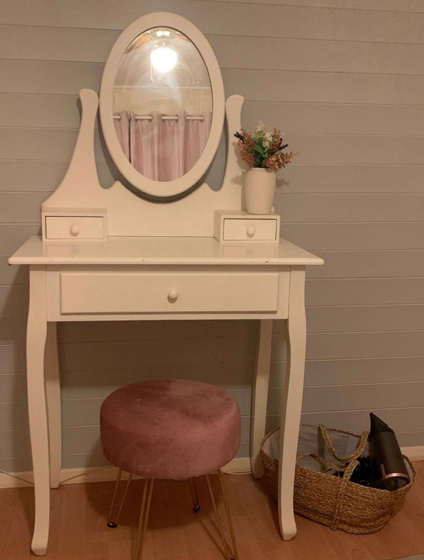 A white vanity with a mirror, two drawers, and a pink stool.
