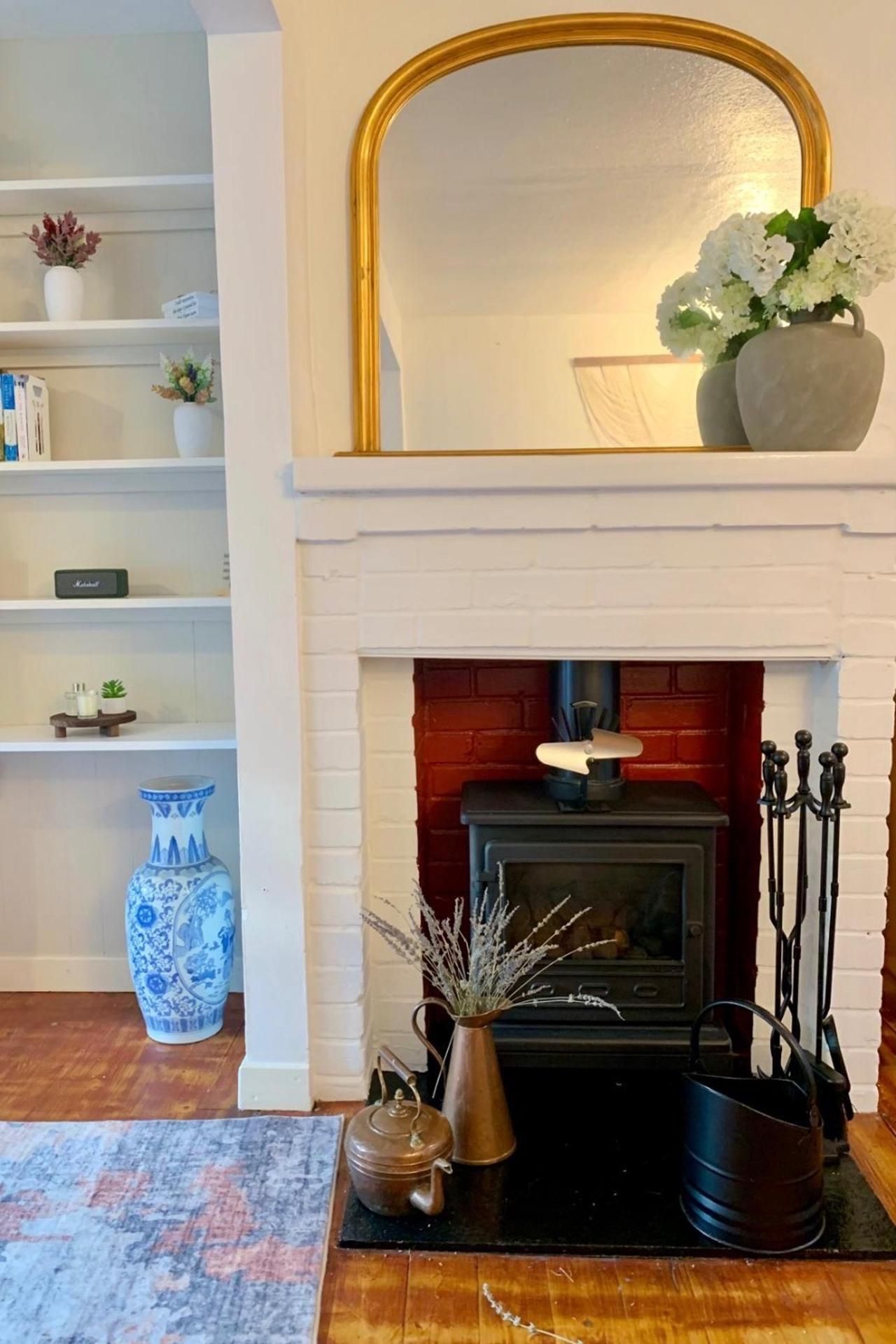 A fireplace with a mantel, a vase with flowers, and a blue and white vase on the floor.