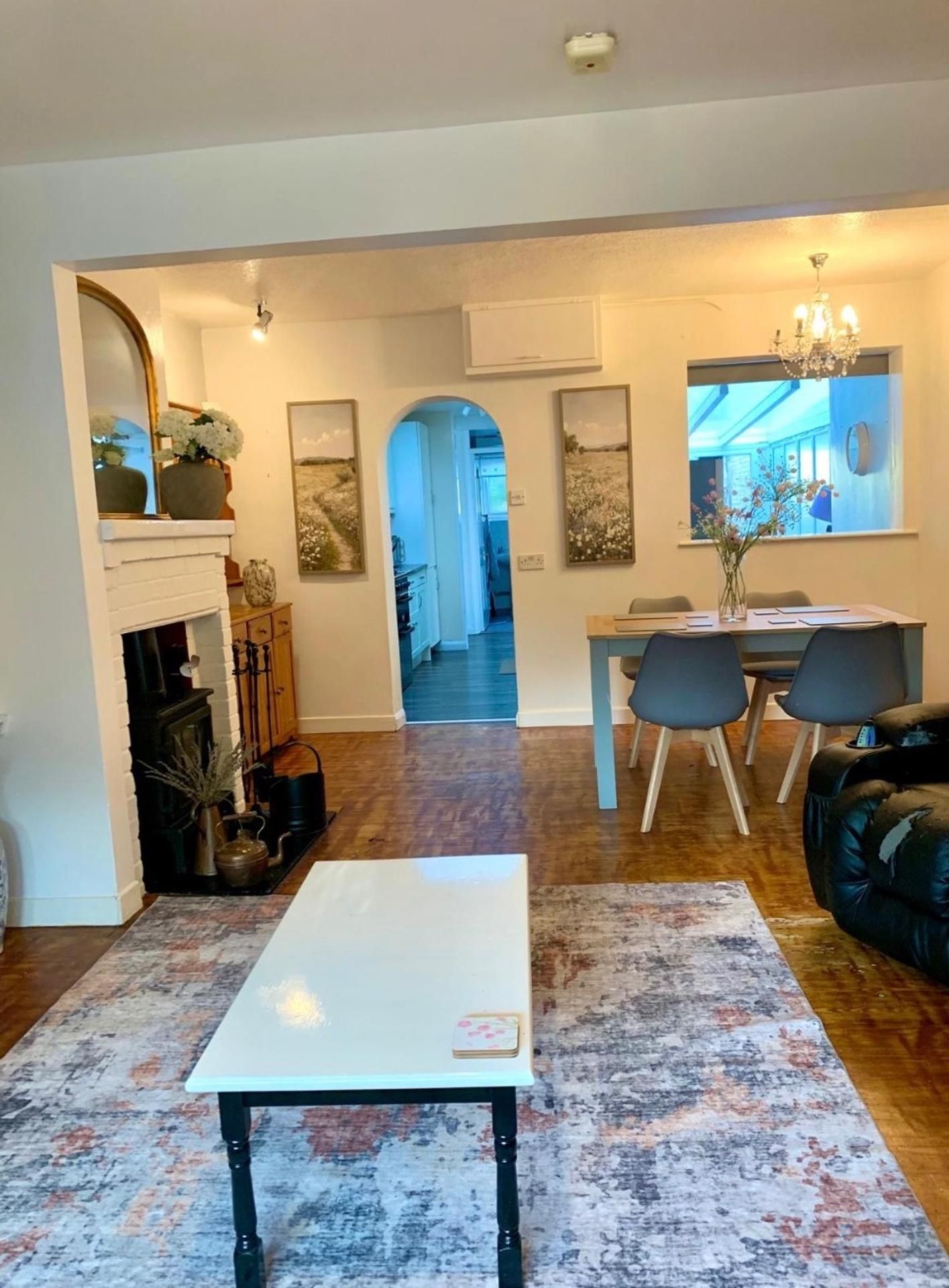 Una sala de estar con chimenea, un comedor con candelabro, y una cocina al fondo.