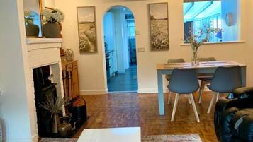Una sala de estar con chimenea, un comedor con candelabro, y una cocina al fondo.