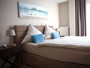 A neatly made bed with a headboard, two bedside lamps, a clock, and a painting on the wall. - Residence by the sea - Strandallee 178 (Timmendorfer Strand)