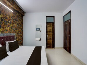 A hotel room with a bed, a headboard, a wall-mounted TV, a door, and a mirror. - Deluxe With Balcony The Cloud inn Hotel Grand (Ghaziabad)