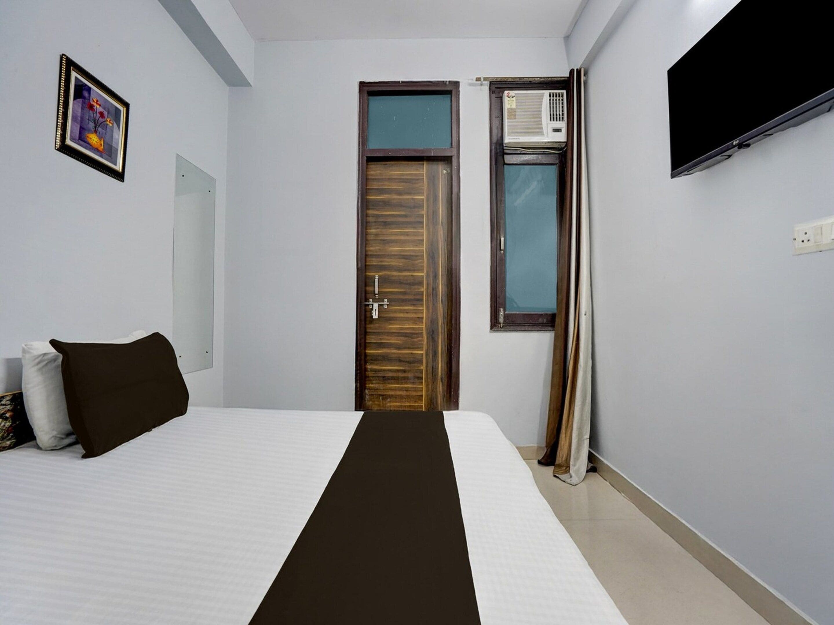 A hotel room with a bed, a door, an air conditioning unit, and a television.