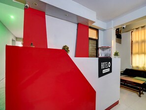Un comptoir d’accueil d’hôtel aux couleurs rouge et blanc, une enseigne indiquant qu’il s’agit d’un hôtel géré par une entreprise, et une fenêtre avec des rideaux.