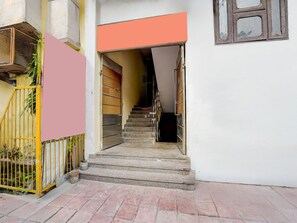 Un escalier menant à l’entrée d’un immeuble, avec une grille en métal et une plante sur le côté gauche.