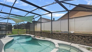 Una piscina de diseño curvo, rodeada por un porche cubierto con pared de piedra y valla.