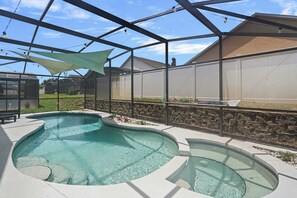 Ein Pool mit geschwungenem Design, umgeben von einer überdachten Terrasse mit einer Steinmauer und einem Zaun.