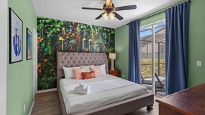 Un dormitorio con una cama grande, un ventilador de techo, una mesita de noche, una lámpara y vistas al exterior a través de un ventanal.