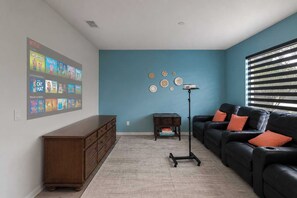 Sala de estar con pared azul, un mueble de madera, un sofá de cuero negro con cojines naranja, una lámpara de pie y un proyector montado en la pared que muestra contenido de Netflix.