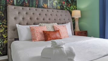 A neatly made bed with white linens and a grey tufted headboard, accompanied by a variety of pillows, including a white one and two with orange polka dots.