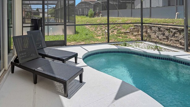 Zona de piscina con dos sillones de descanso y un porche con paredes de vidrio.