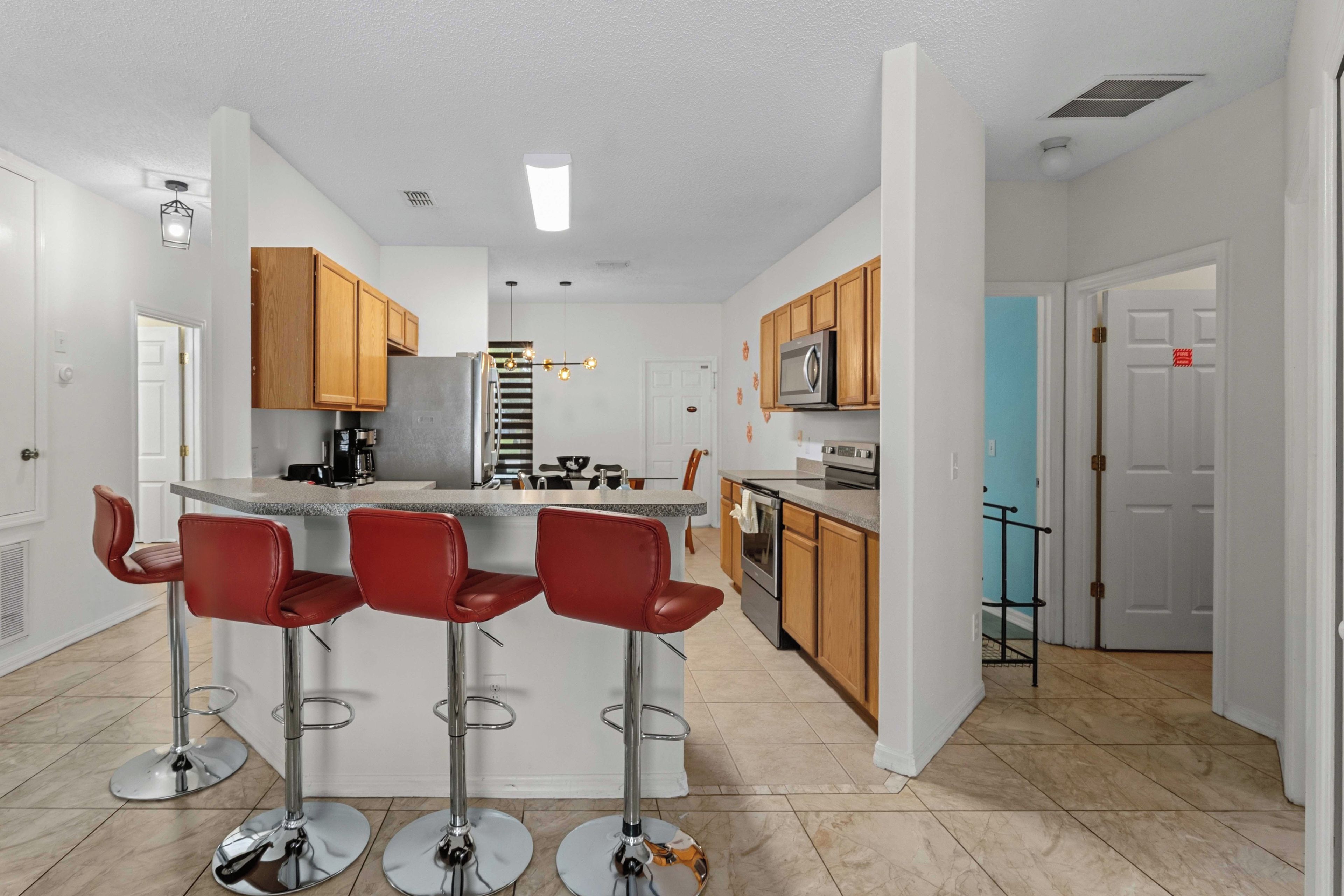A modern kitchen with a central island, bar stools, wooden cabinets, and stainless steel appliances.