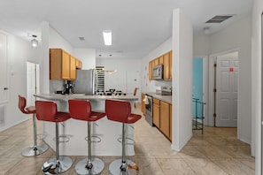 Una cocina moderna con una isla central, taburetes de bar, armarios de madera y electrodomésticos de acero inoxidable.