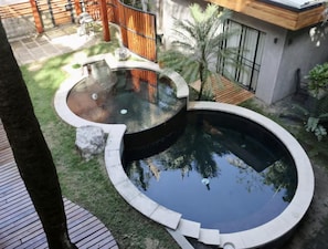 A circular hot tub with a stone border, surrounded by a wooden deck and a grassy area with palm trees. - Casa Palmera: Brand-New 4BR Villa w/ Pool, 5-Min Walk to Beach (Nosara)