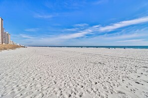 A wide sandy beach with footprints, a clear sky, and a distant view of a building. - The Pelican Nest-Perfect North Myrtle Beach Getaway (MYRTLE BEACH)
