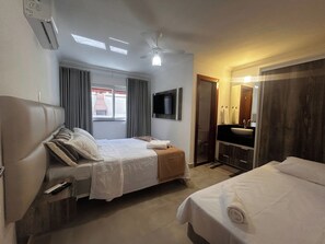 A hotel room with two beds, a ceiling fan, a TV, a window with curtains, a bathroom with a sink and mirror, and a wooden door. - CJ17GIL -3D -Arraial D’ajuda/Piscina/ Beach Tennis (Arraial da Ajuda)