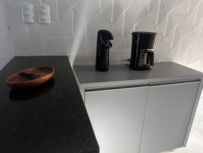 A kitchen with a black countertop, a wooden bowl, a black coffee maker, and a silver cabinet. - CJ17GIL -3D -Arraial D’ajuda/Piscina/ Beach Tennis (Arraial da Ajuda)