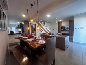 A modern dining area with a wooden table set for four, a staircase, and a flat-screen TV mounted on the wall. - CJ17GIL -3D -Arraial D’ajuda/Piscina/ Beach Tennis (Arraial da Ajuda)