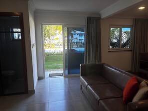 A living room with a leather sofa, a door leading outside, and a window with curtains. - CJ17GIL -3D -Arraial D’ajuda/Piscina/ Beach Tennis (Arraial da Ajuda)