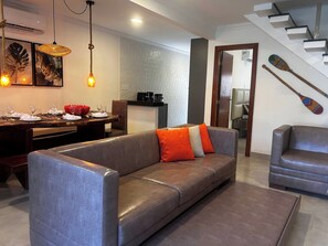 Ein modernes Wohnzimmer mit einem grauen Sofa, einem Essbereich mit einem Holztisch, der für eine Mahlzeit gedeckt ist, und einer Treppe mit Holzstufen.