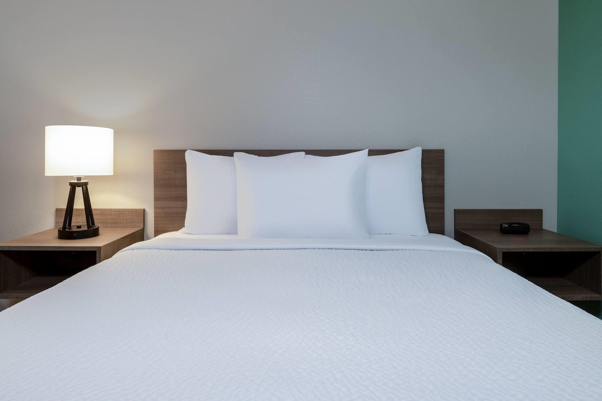 Una habitación de hotel con una cama bien hecha, una lámpara de noche y una mesita de noche con un teléfono.