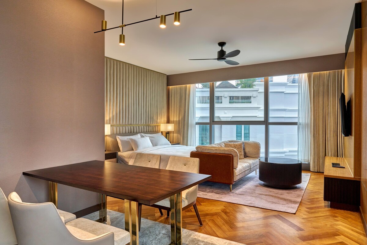 A modern hotel room with a bed, a sofa, a dining table, and a TV.