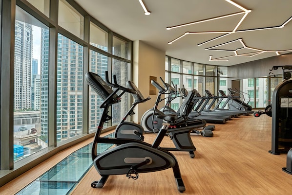 A gym with multiple treadmills and exercise bikes, large windows with a city view, and a modern ceiling design.