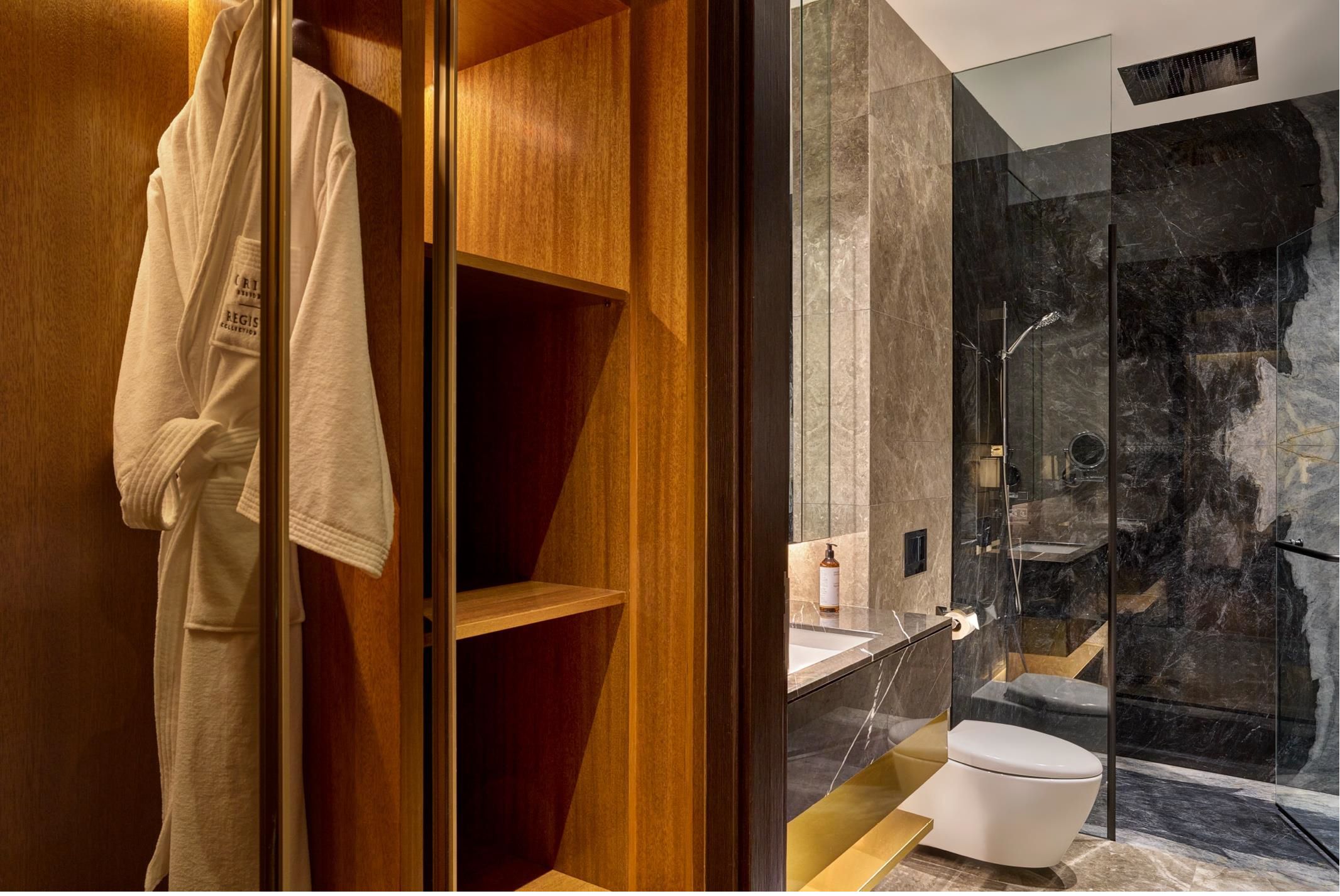 Un baño moderno con cabina de ducha de vidrio, tocador de madera y una bata colgada en la puerta.