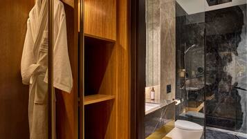 Un baño moderno con cabina de ducha de vidrio, tocador de madera y una bata colgada en la puerta.