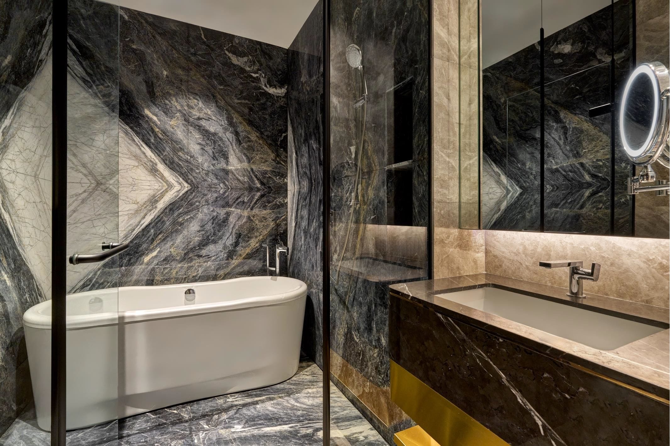 Un baño moderno con una bañera independiente, un tocador con espejo y paredes de mármol.