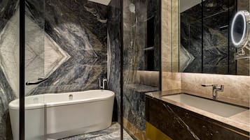 Un baño moderno con una bañera independiente, un tocador con espejo y paredes de mármol.
