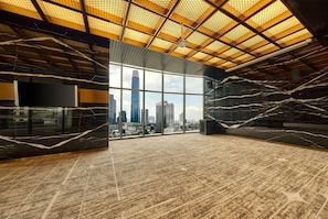 A spacious room with a large window offering a city view, a modern ceiling design, and a marble floor.