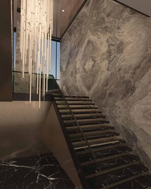 A modern staircase with a marble wall and a hanging light fixture.